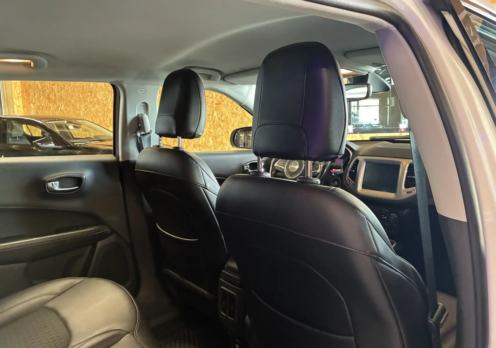 Vue intérieure arrière du Jeep Compass ivoire 2021, montrant sièges avant en cuir noir et tableau de bord avec écran tactile.