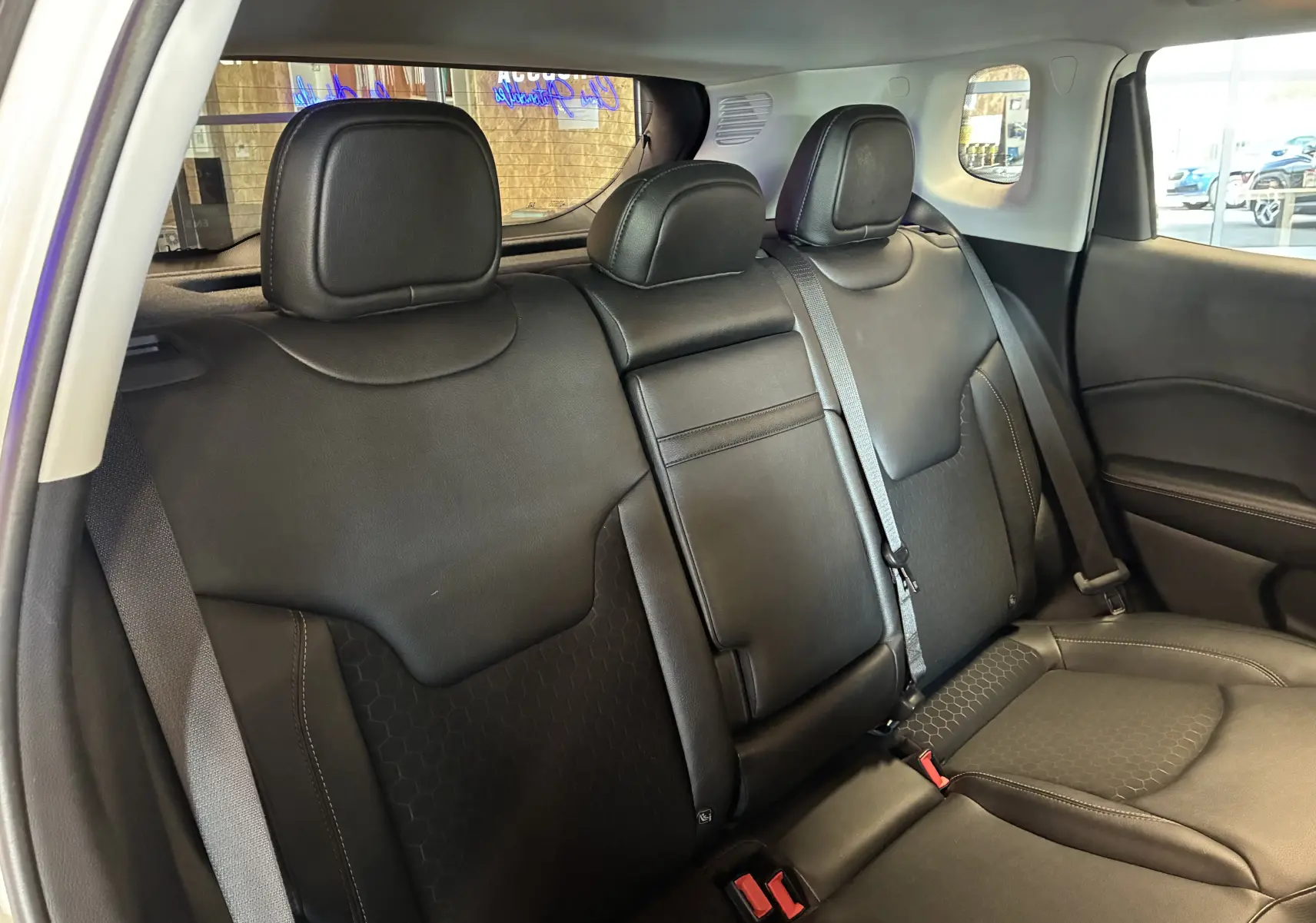 Vue intérieure arrière du Jeep Compass 2021, sièges en cuir noir avec accoudoir central rabattable et ceintures visibles.