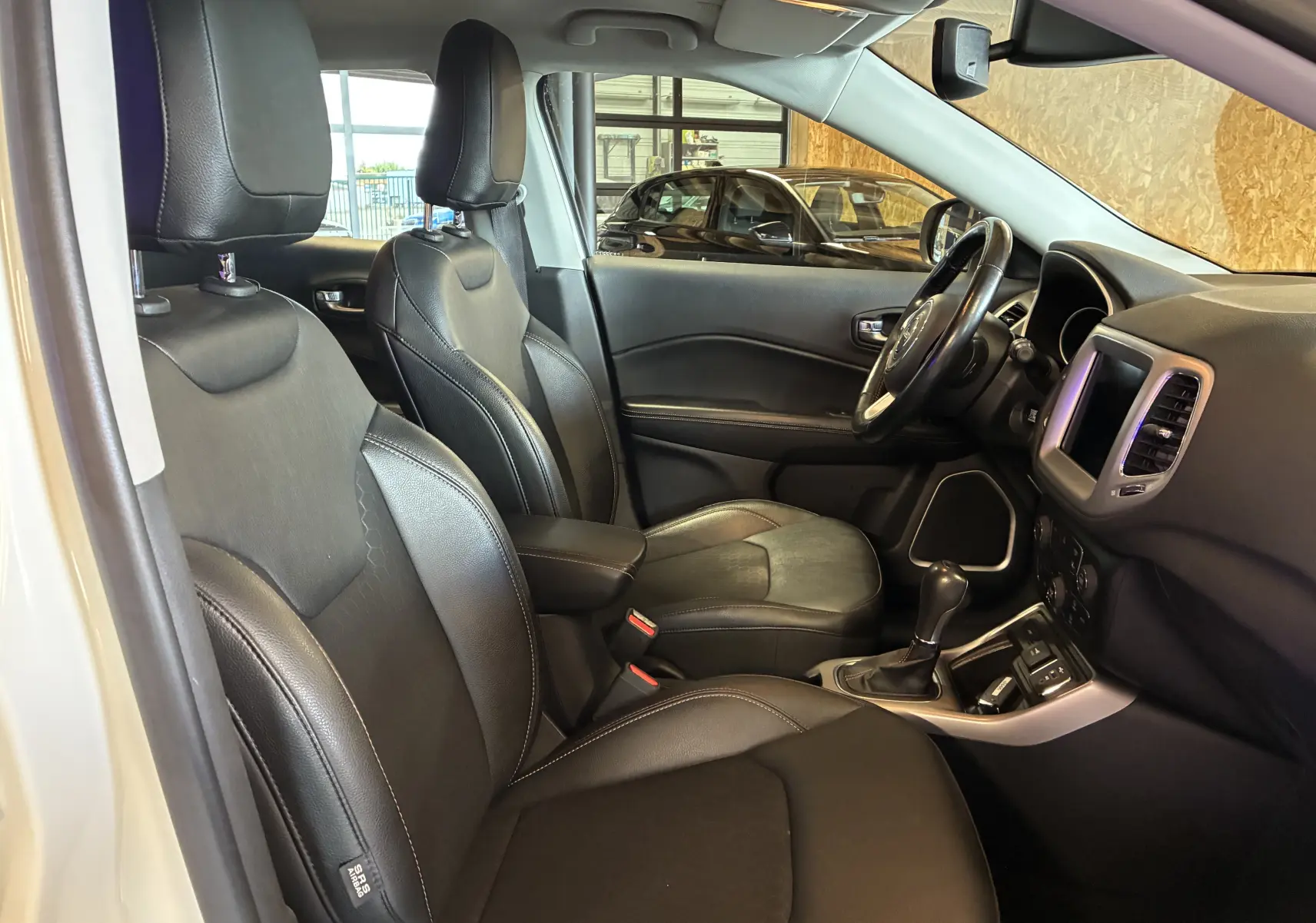 Vue intérieure côté conducteur du Jeep Compass ivoire 2021, sièges cuir noirs et console centrale avec boîte auto.