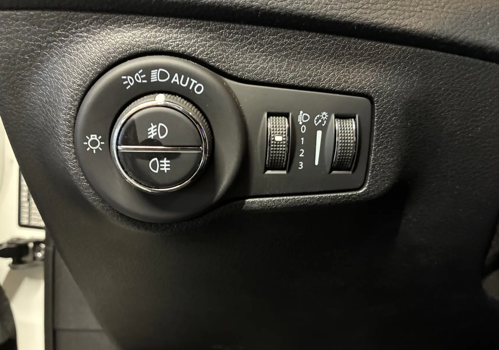 Gros plan sur les commandes d’éclairage noires du tableau de bord du Jeep Compass ivoire, avec réglages automatiques et antibrouillard.