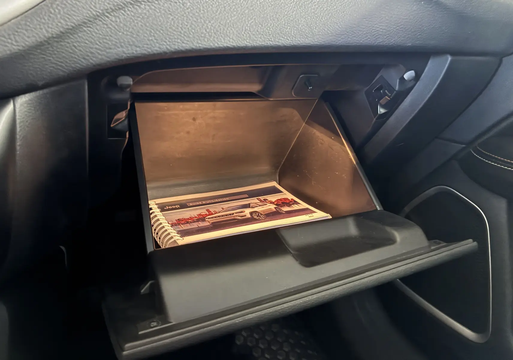 Gant de boîte à gants ouvert côté passager du Jeep Compass ivoire, montrant un manuel d'utilisation à l'intérieur.