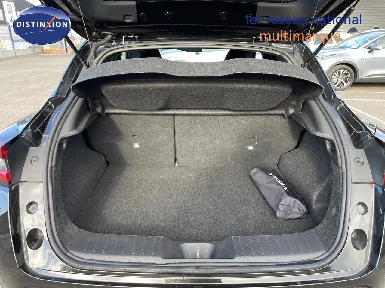 Coffre ouvert d'un Nissan Juke noir métal 2024, montrant un espace de chargement propre avec un sac Nissan à droite.