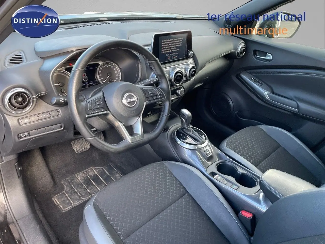 Intérieur du Nissan Juke 2024 noir métal, vue côté conducteur montrant le tableau de bord et la console centrale moderne.