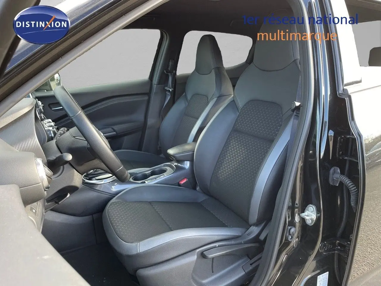 Intérieur avant droit du Nissan Juke 2024 noir métal, sièges en cuir gris et tableau de bord visible.