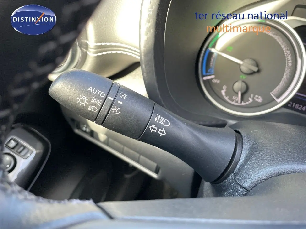 Gros plan sur la commande des phares et clignotants du Nissan Juke 2024 noir métal, avec tableau de bord hybride en arrière-plan.