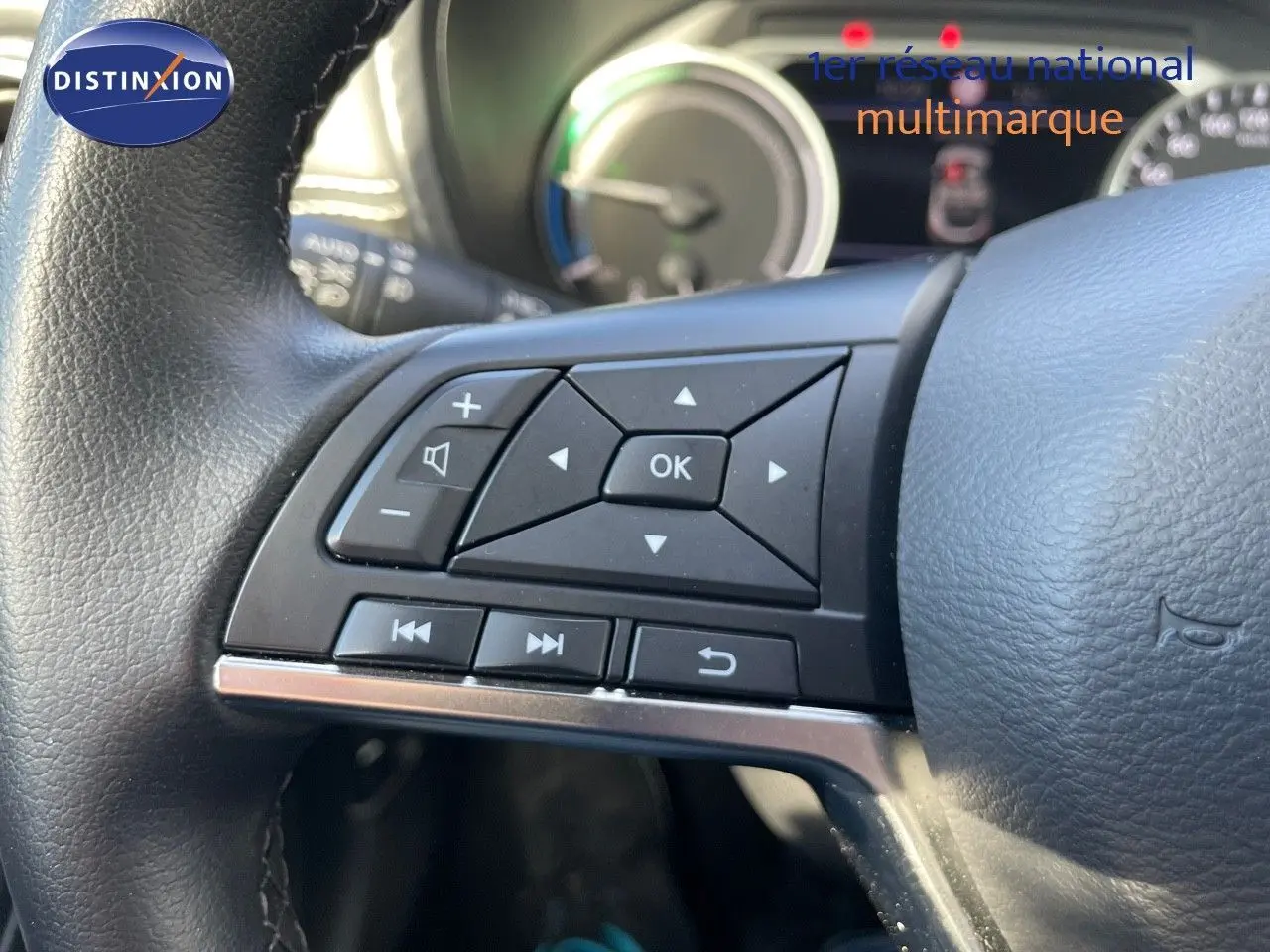 Gros plan sur les commandes multifonctions à gauche du volant noir du Nissan Juke 2024 hybride, tableau de bord en arrière-plan.