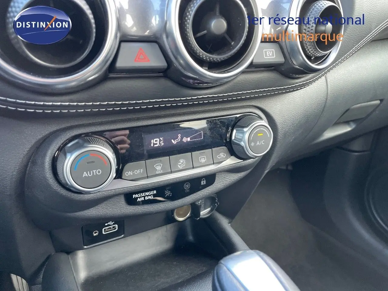 Console centrale du Nissan Juke 2024 en noir métal, vue rapprochée du tableau de bord avec commandes climatisation et prise USB.