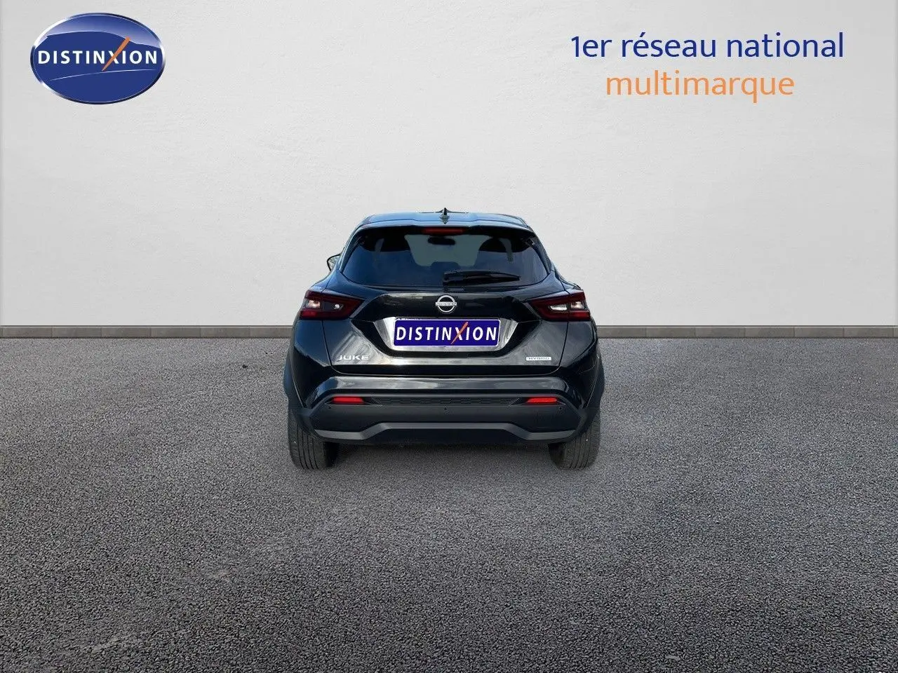 Vue arrière d'un Nissan Juke noir métal 2024, version hybride, garé sur un sol gris devant un mur blanc.