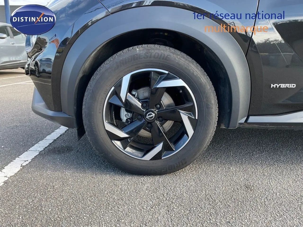 Gros plan sur la roue avant gauche noire métallisée du Nissan Juke 2024 hybride avec jante biton et logo Nissan visible.