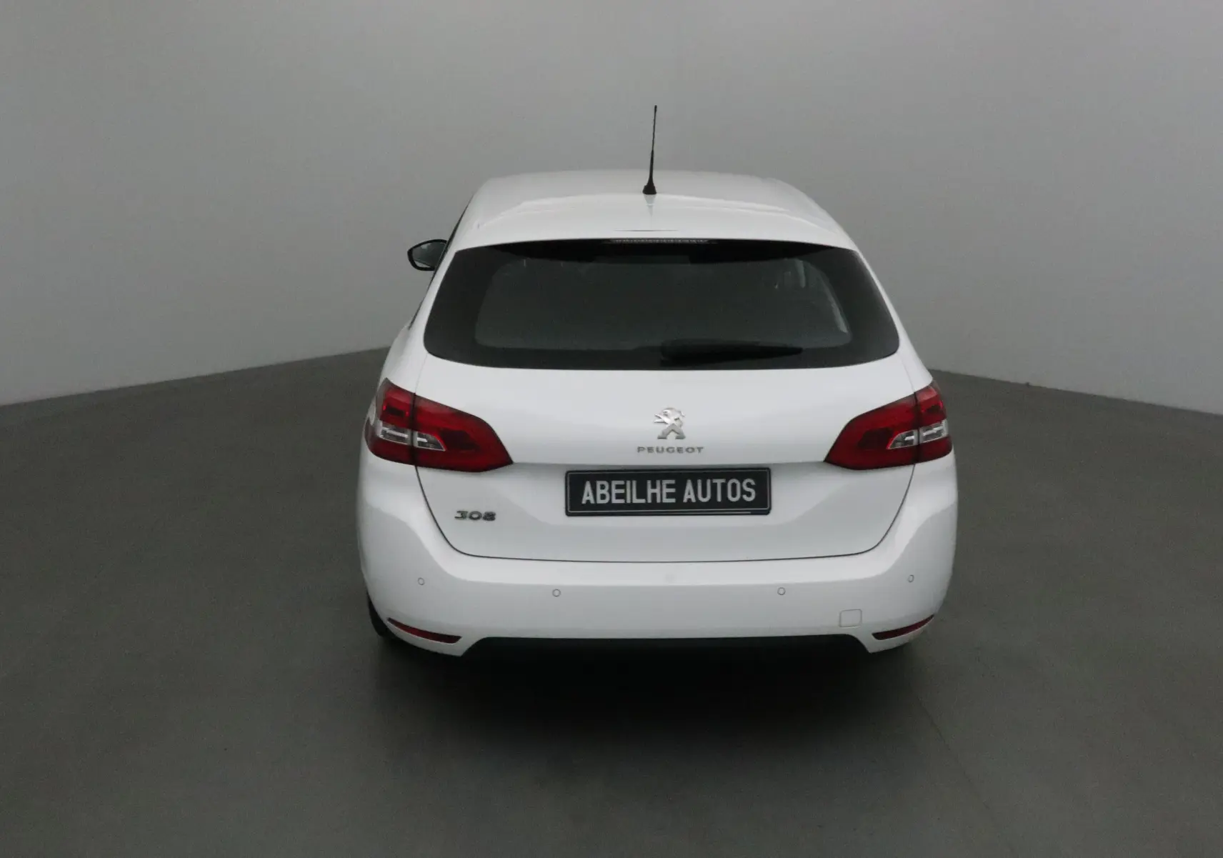Vue arrière d'une Peugeot 308 SW blanche de 2018 avec feux arrière rouges et plaque Abeilhe Autos.