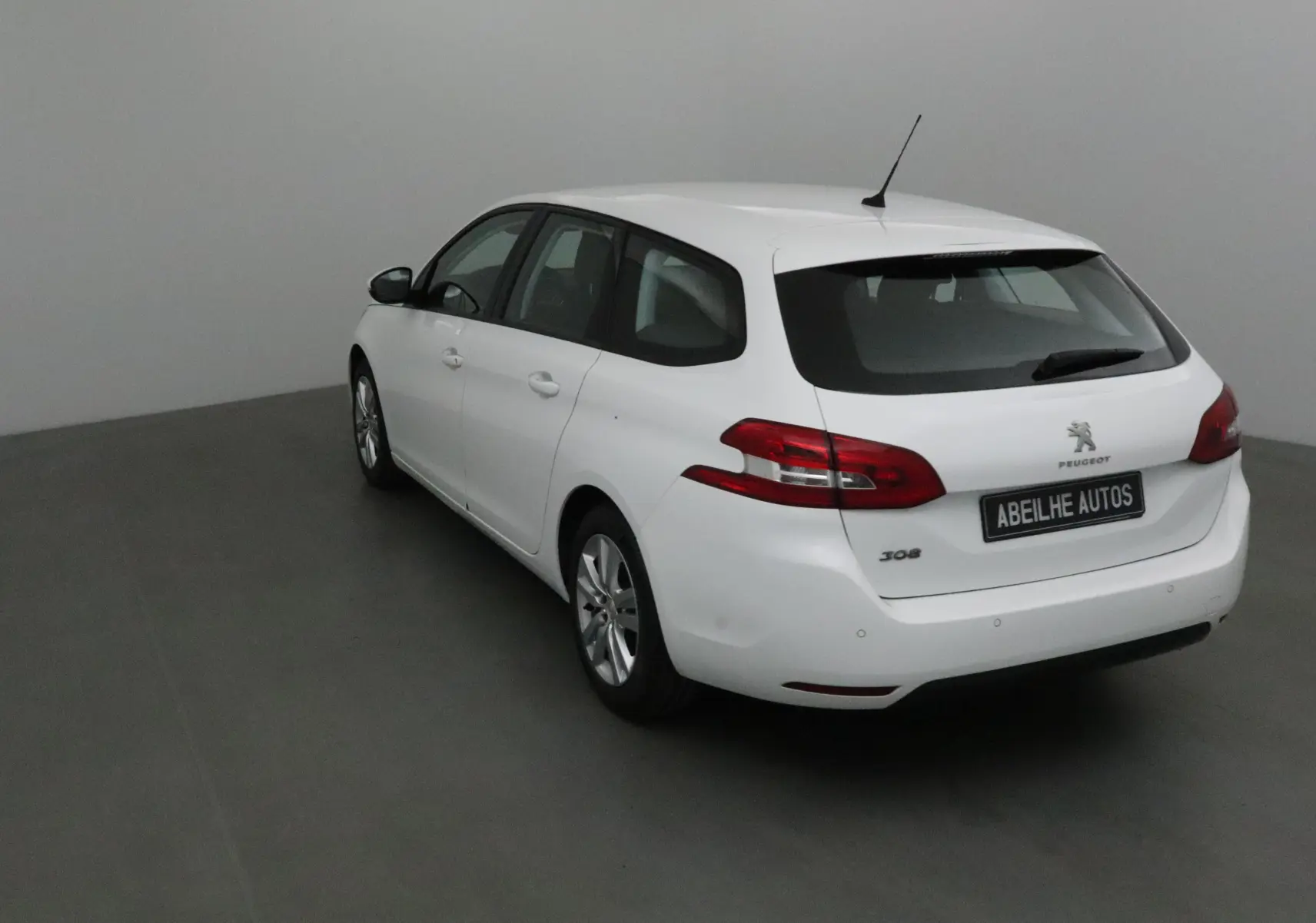 Peugeot 308 SW blanche vue en 3/4 arrière droit, avec feux arrière rouges et antenne de toit visible.