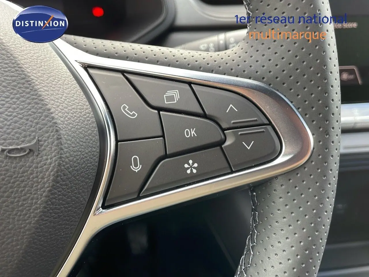 Gros plan sur les commandes multifonctions à droite du volant perforé d'un Renault Captur rouge passion 2025.