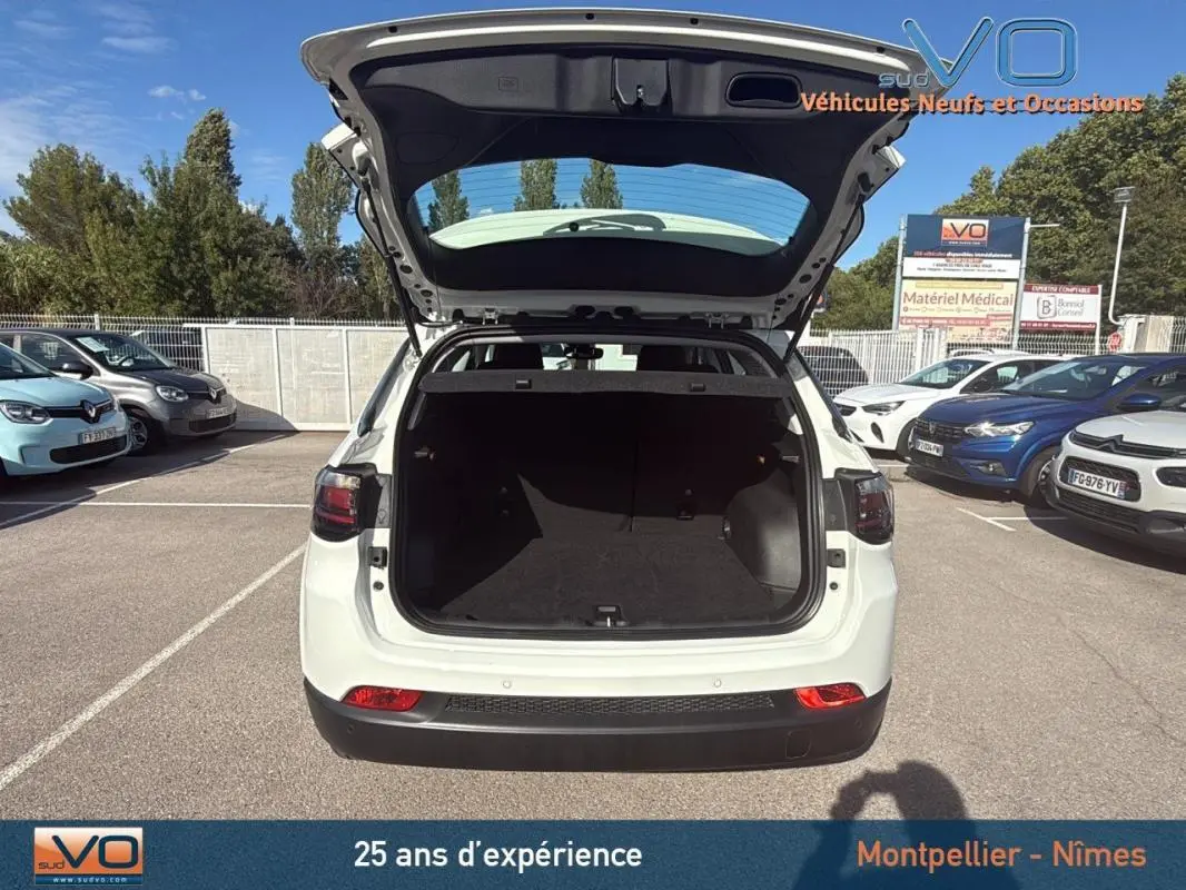 Vue arrière ouverte du Jeep Compass blanc 2024 montrant le coffre spacieux dans un parking extérieur.