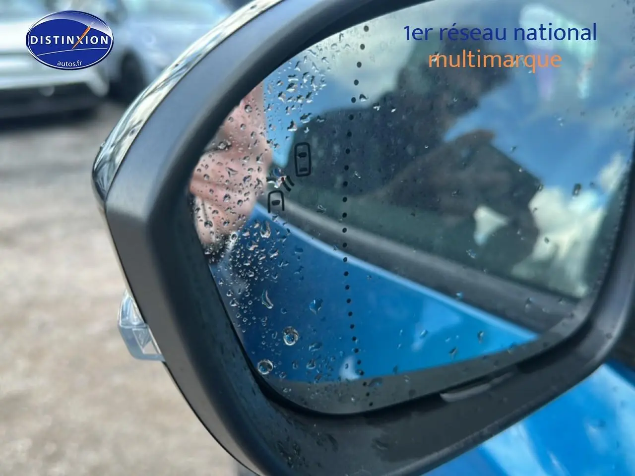 Rétroviseur droit de Renault Austral bleu 2026 avec gouttes d'eau et indicateur d'angle mort visible.