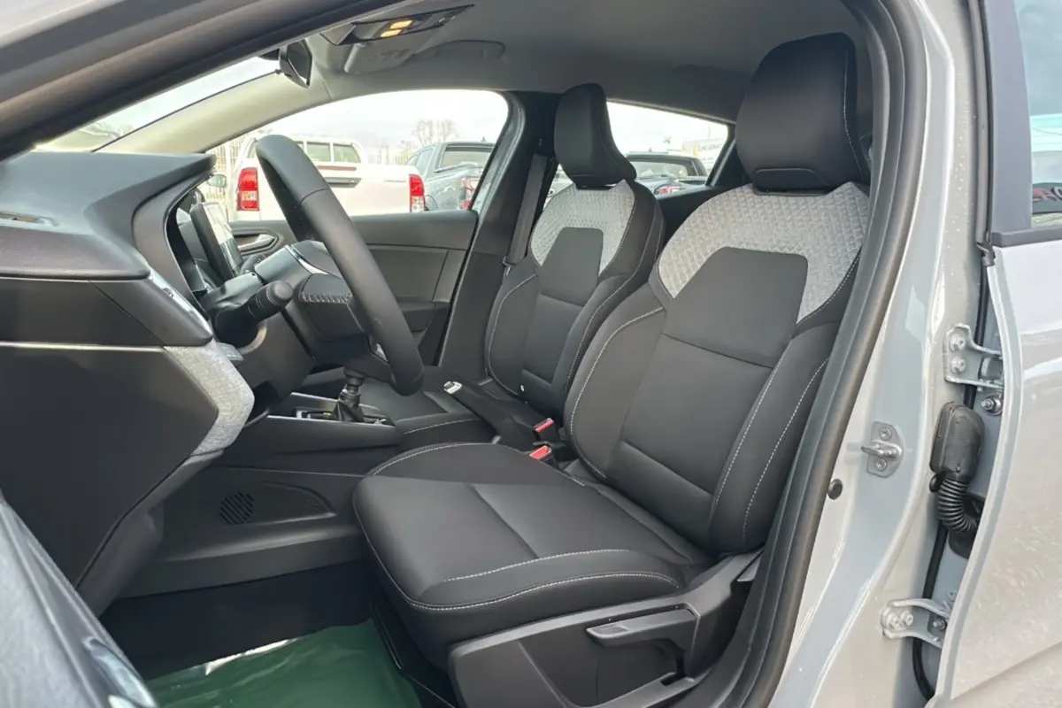 Vue intérieure côté conducteur de la Renault Clio gris rafale 2025, sièges avant en tissu noir et gris, volant multifonctions.