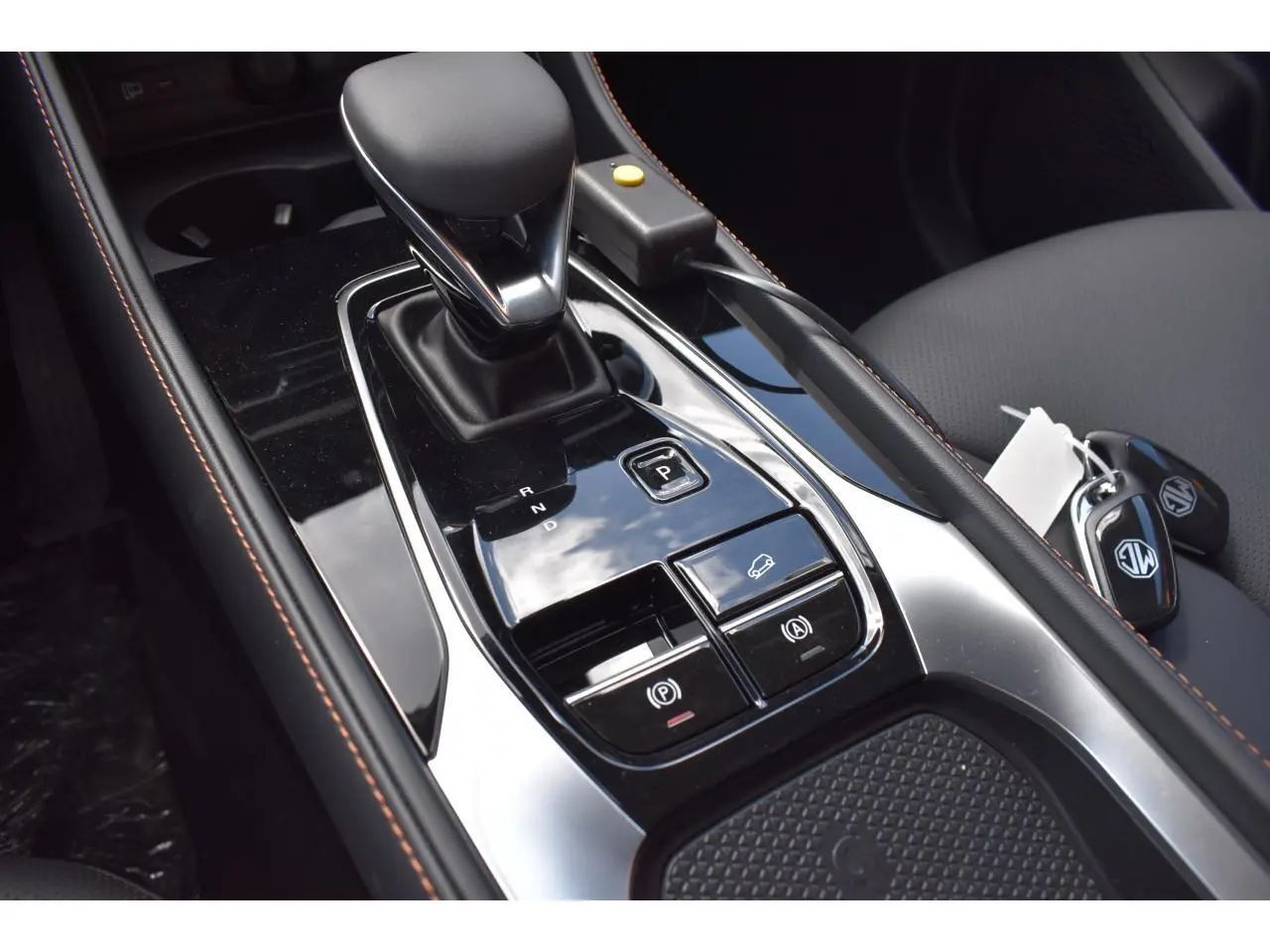 Gros plan sur la console centrale noire brillante du MG Motor EHS gris, avec levier de vitesse automatique et clés visibles.
