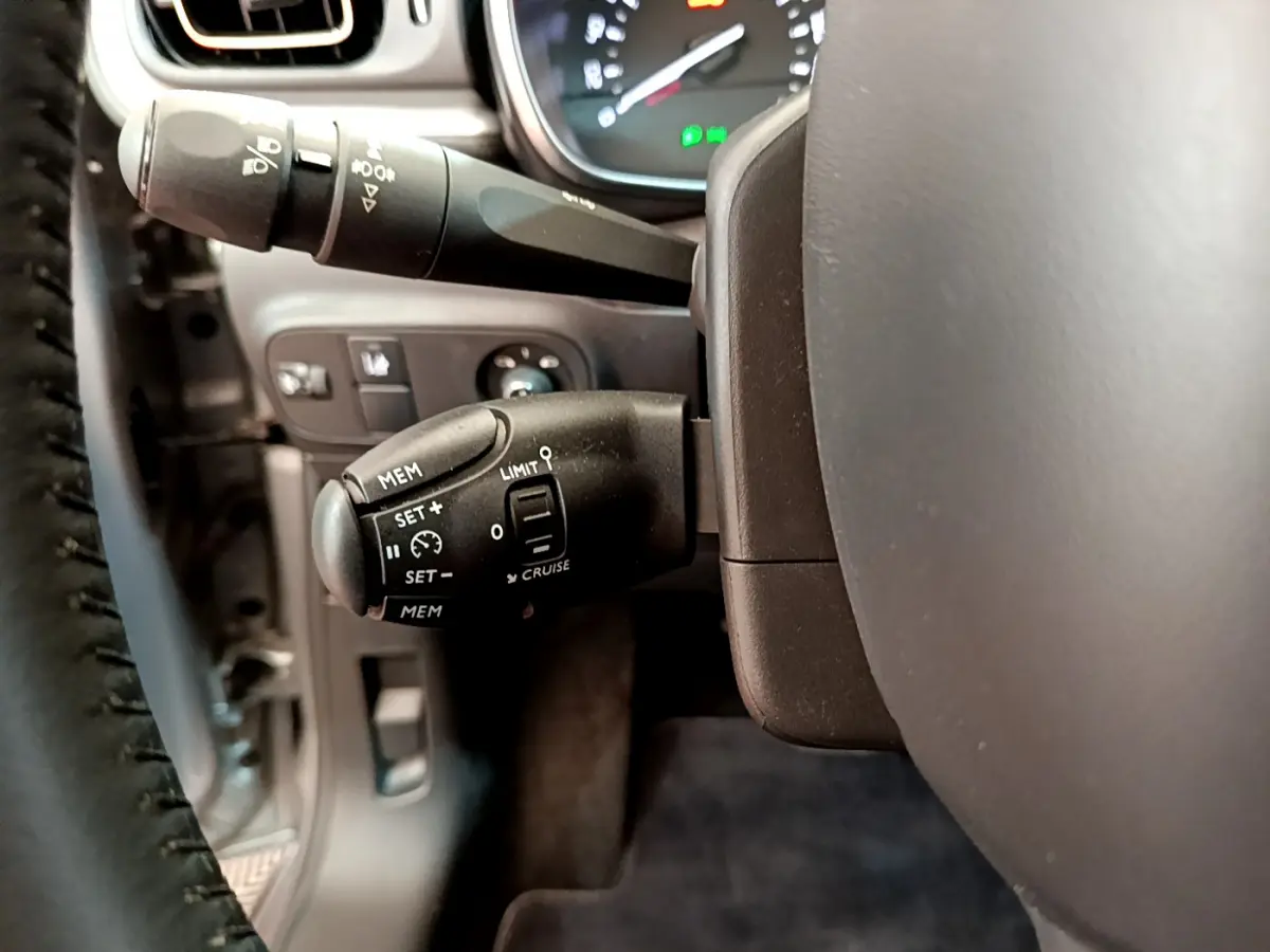 Gros plan sur la commande de régulateur de vitesse à gauche du volant cuir d'une Citroën C3 gris clair 2019.