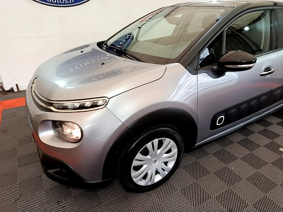 Citroën C3 gris clair vue 3/4 avant droit, avec protections latérales noires et jantes argentées.