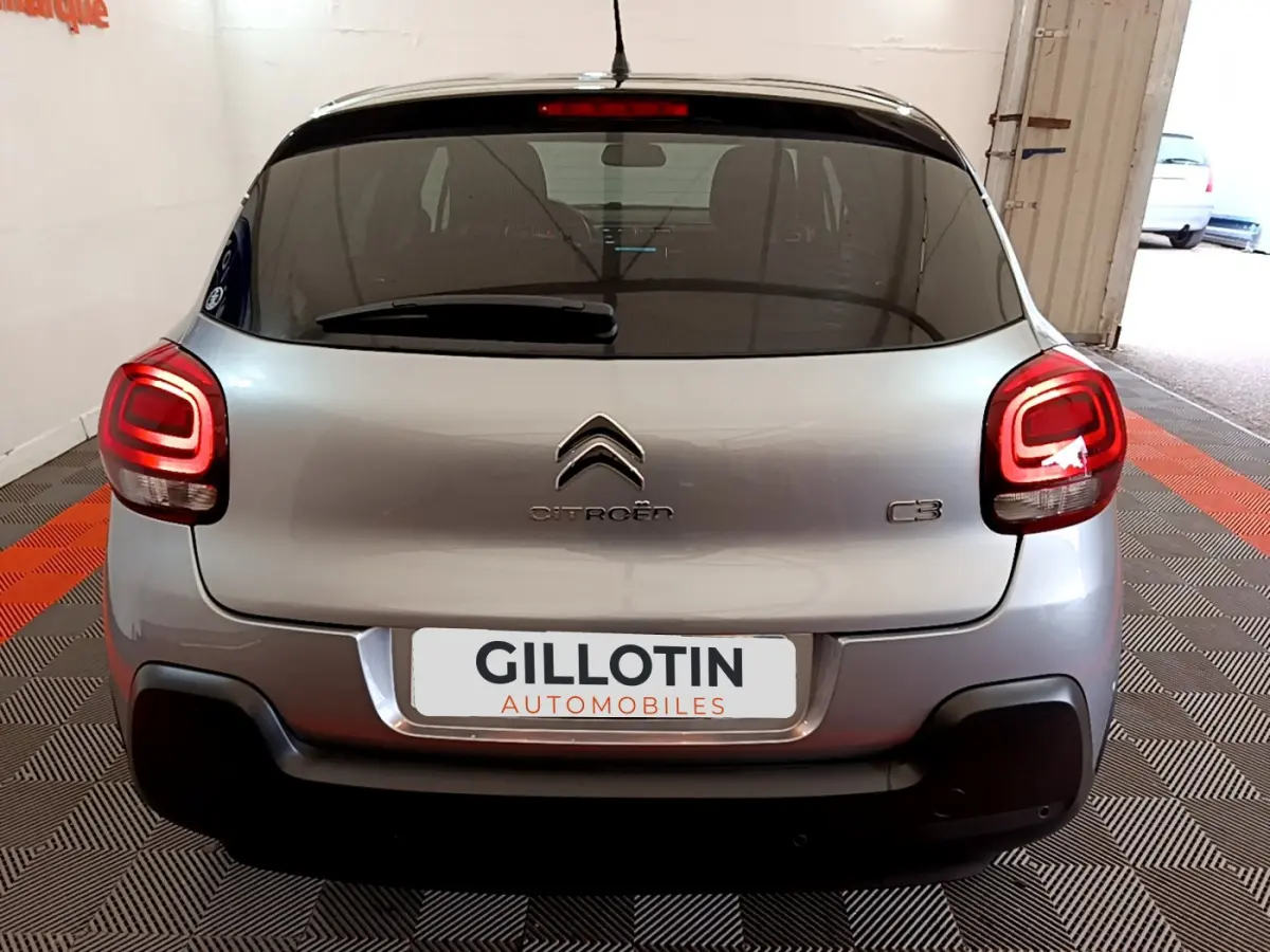 Vue arrière d'une Citroën C3 gris clair avec feux arrière allumés dans un garage intérieur.