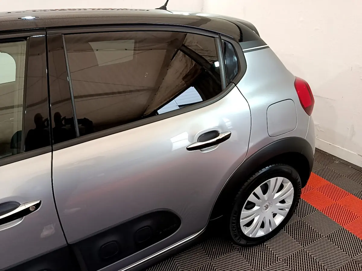 Vue latérale côté droit d'une Citroën C3 gris clair avec poignées chromées et jantes acier sur tapis bicolore.