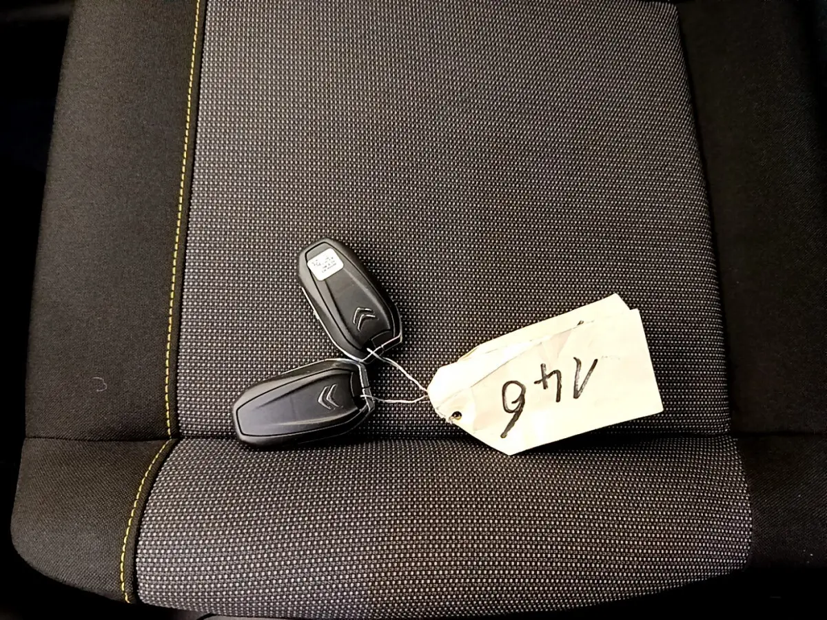 Gros plan sur deux clés noires Citroën posées sur un siège gris foncé avec surpiqûres jaunes.