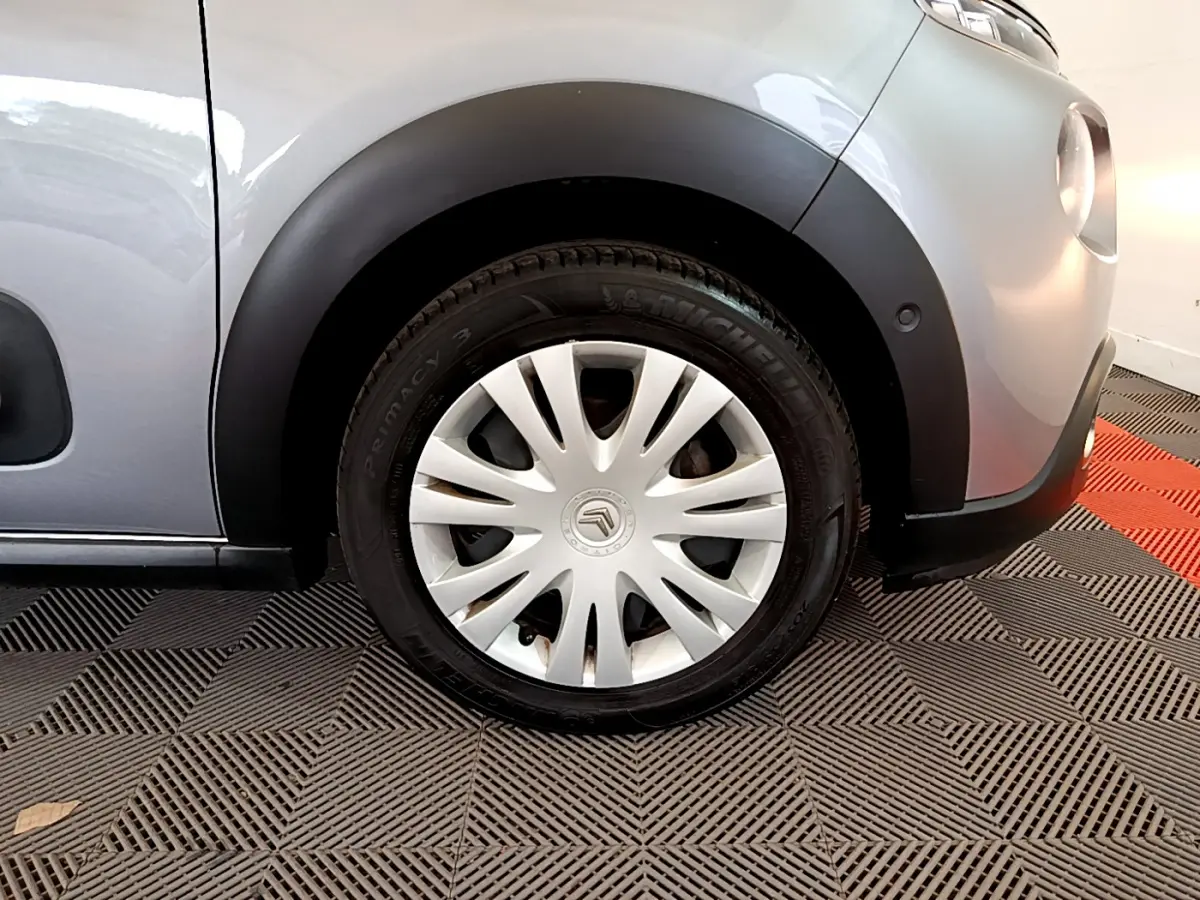 Gros plan sur la roue avant droite d'une Citroën C3 gris clair, avec jante en acier et enjoliveur blanc.