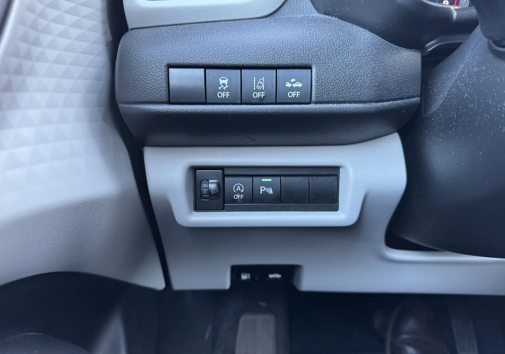 Vue rapprochée des commandes situées sous le volant côté gauche d'une Suzuki Swift 2024 blanc/gris hybride.