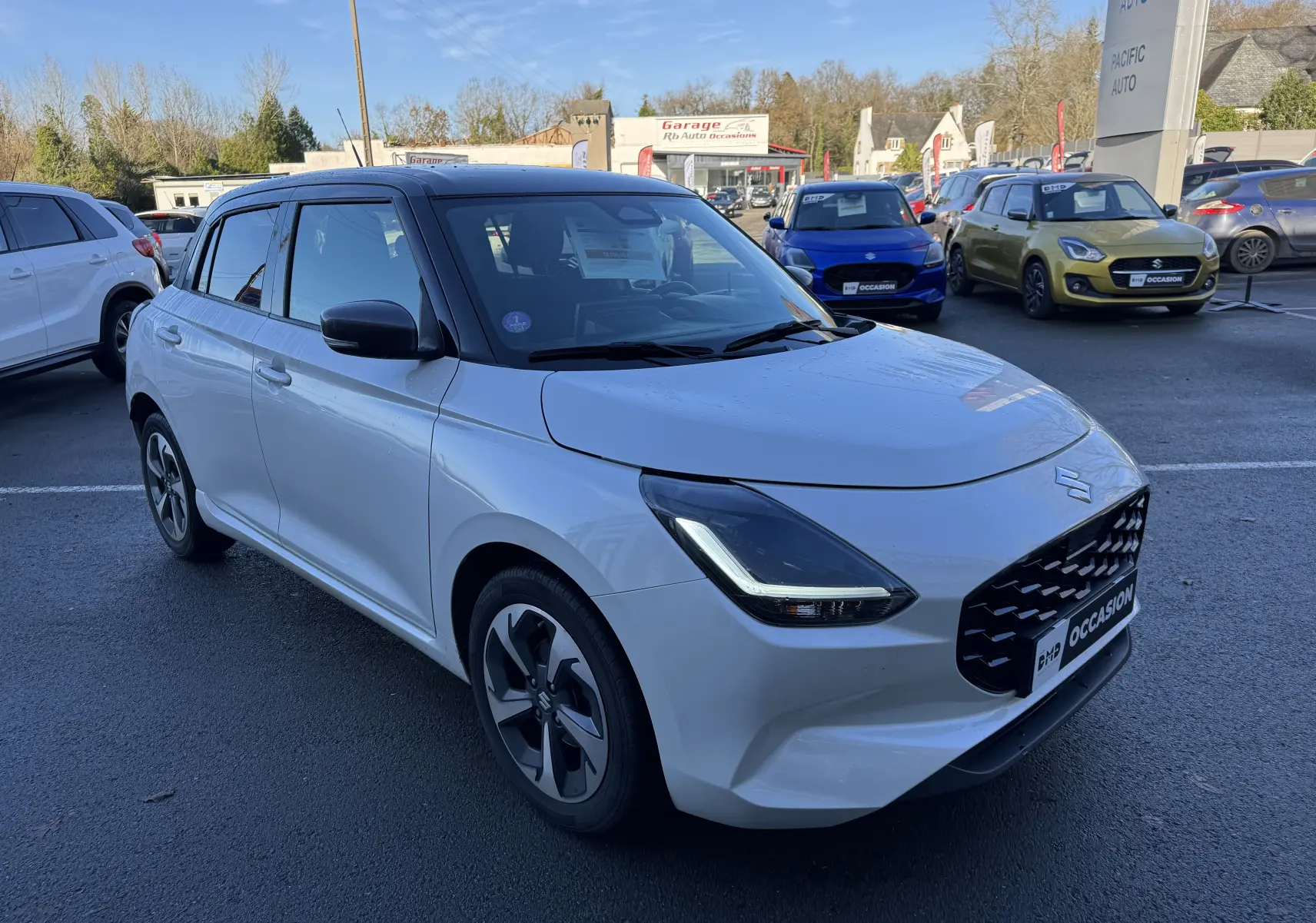 Suzuki Swift 2024 hybride blanc et gris vue 3/4 avant droit sur parking de concession.