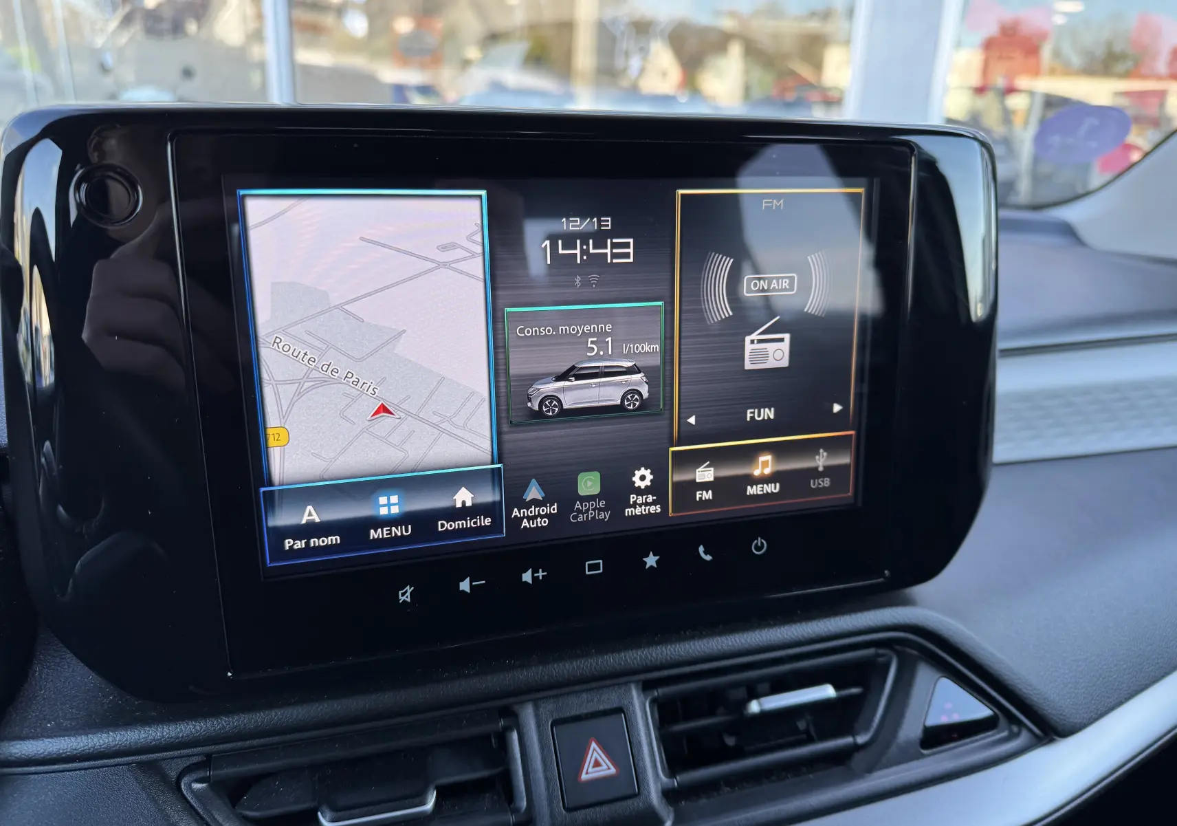 Écran tactile central de la Suzuki Swift 2024 affichant navigation, consommation hybride et radio FM en intérieur.