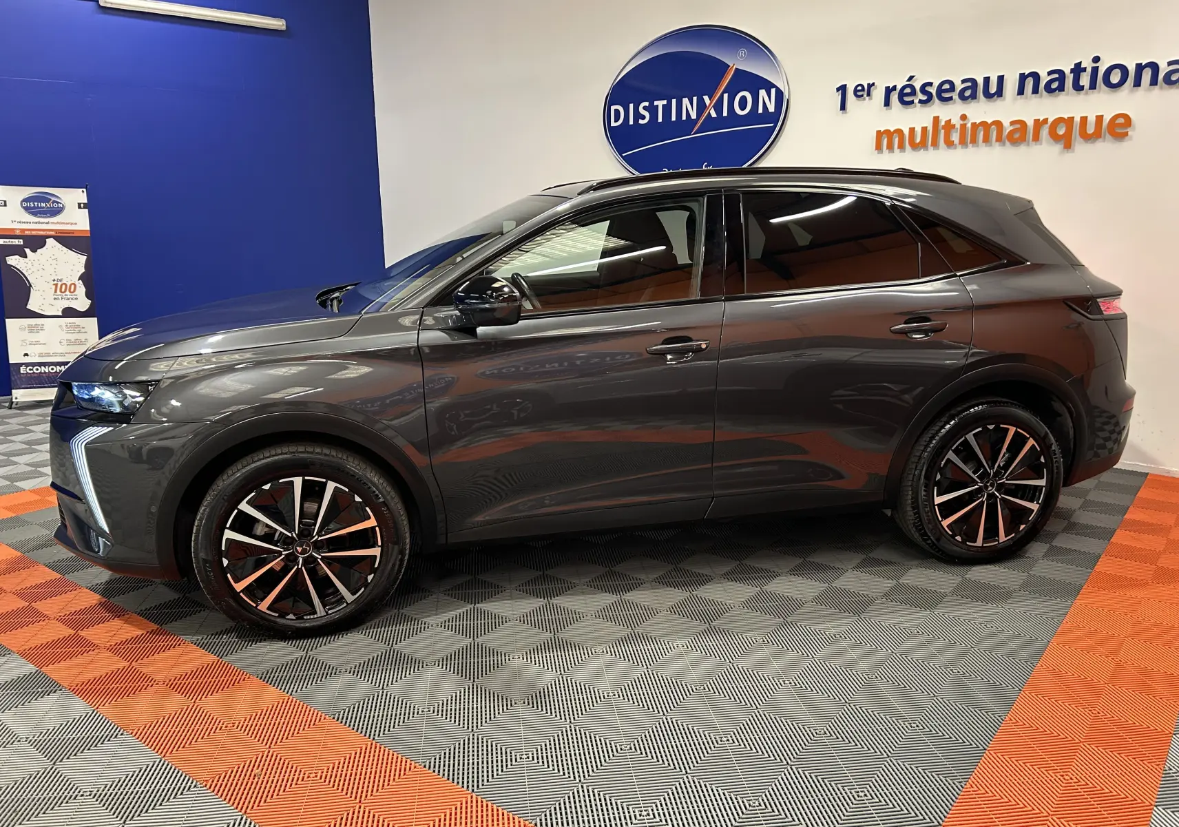 Vue de profil côté gauche du SUV DS7 BlueHDi 130 gris titane avec jantes bi-ton et hayon électrique en intérieur showroom.