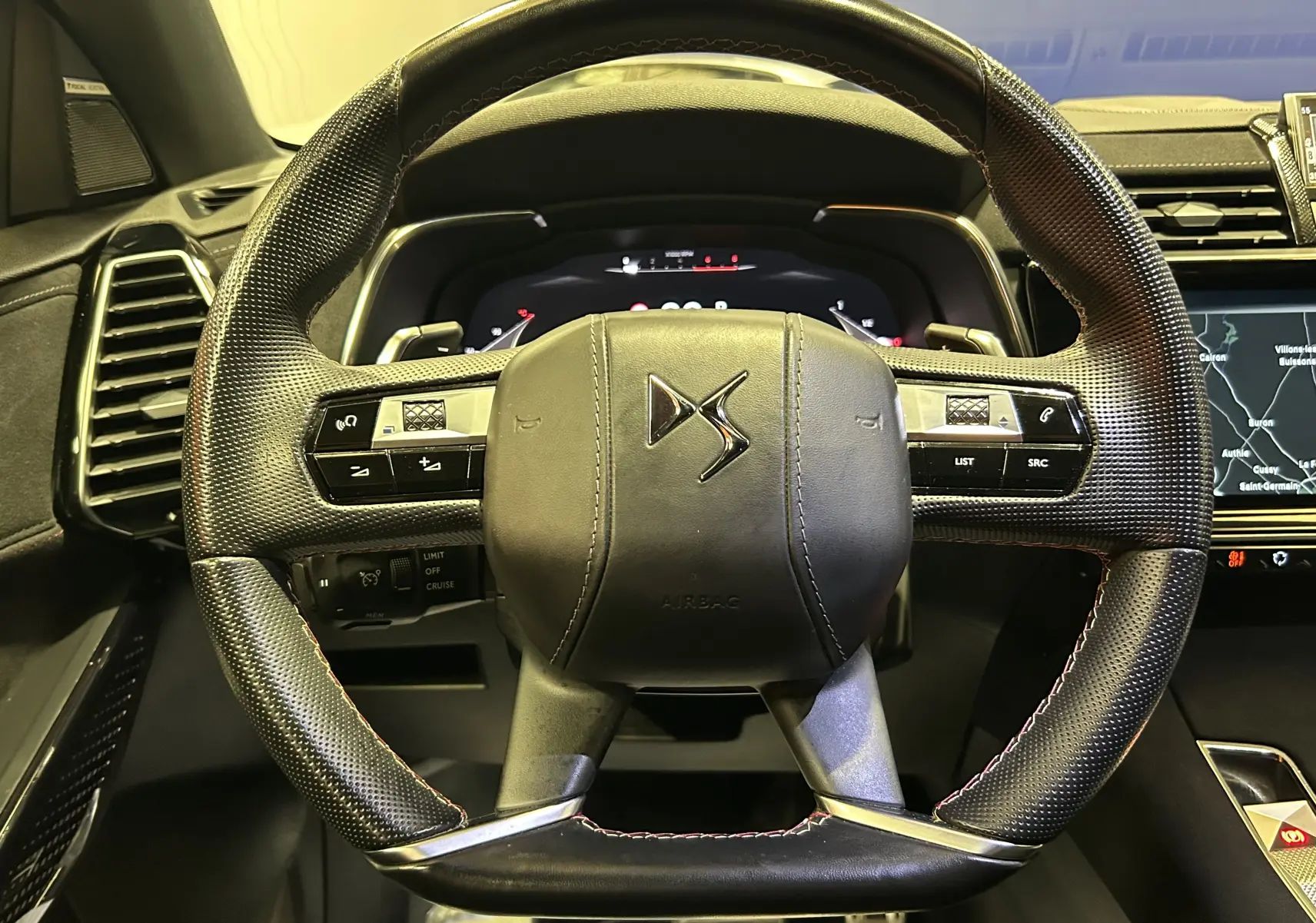 Vue rapprochée du volant en cuir perforé noir avec logo DS, tableau de bord numérique et écran tactile visible à droite.