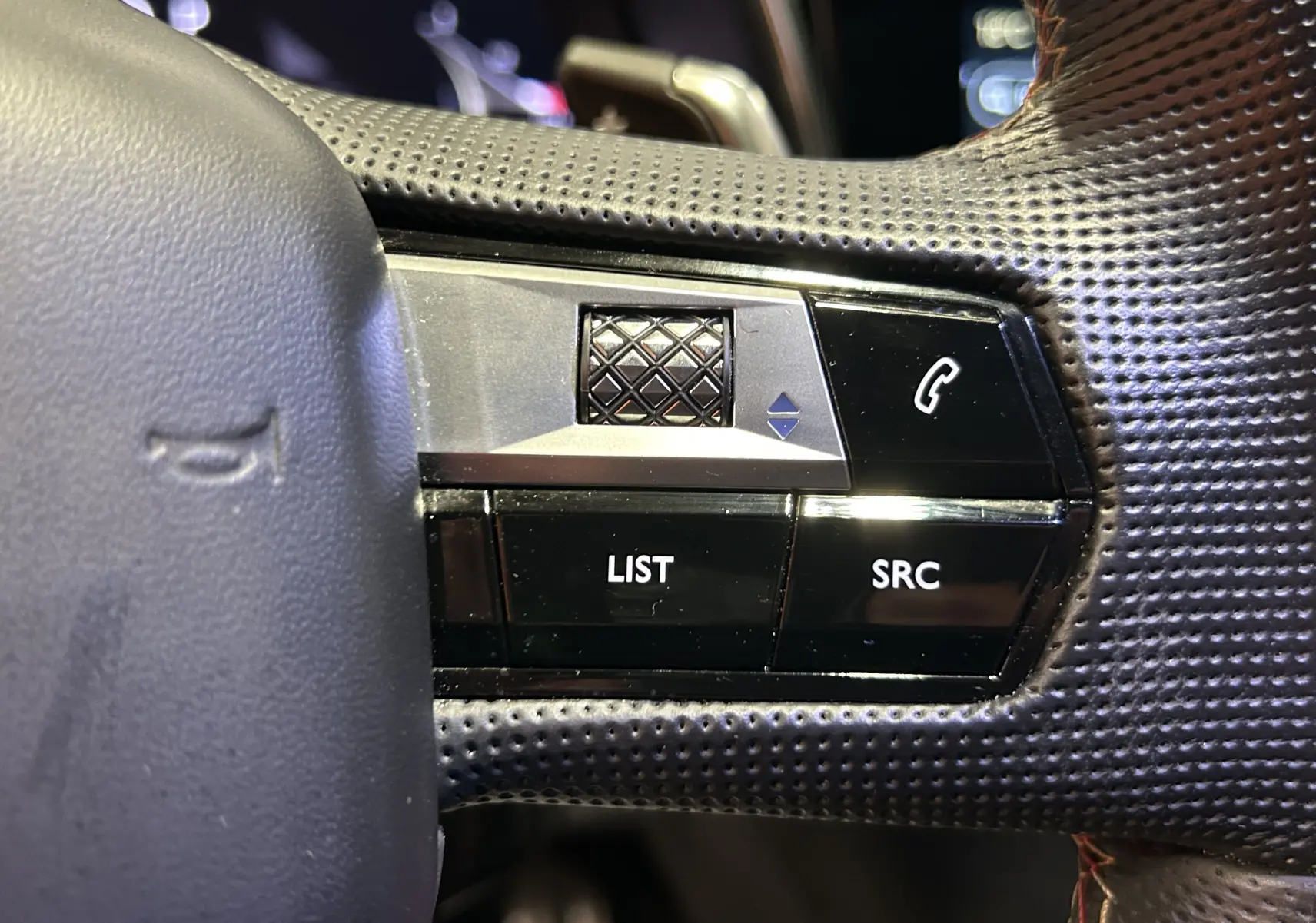 Gros plan sur les commandes gauche du volant perforé du DS7 2024 gris titane, avec boutons LIST, SRC et symbole téléphone.