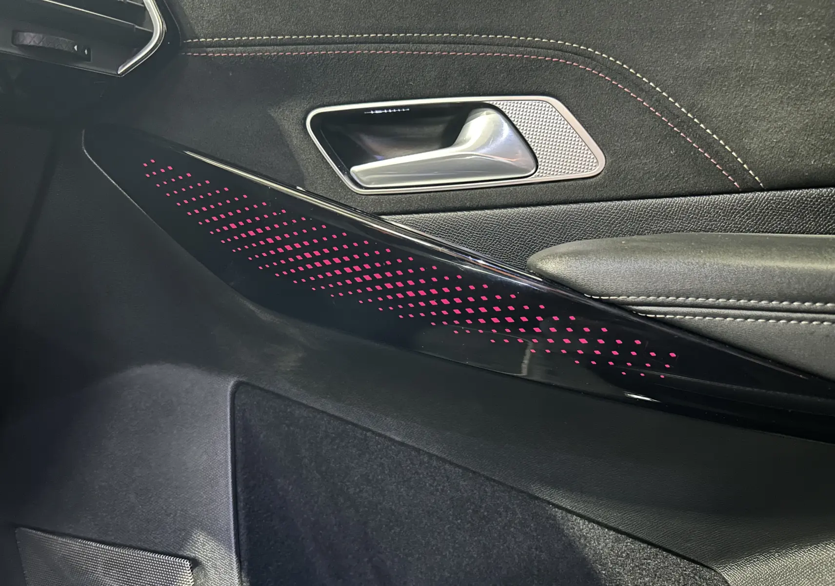 Détail de la porte côté gauche du DS7 2024 avec éclairage d’ambiance rose et surpiqûres rouges sur le revêtement noir.