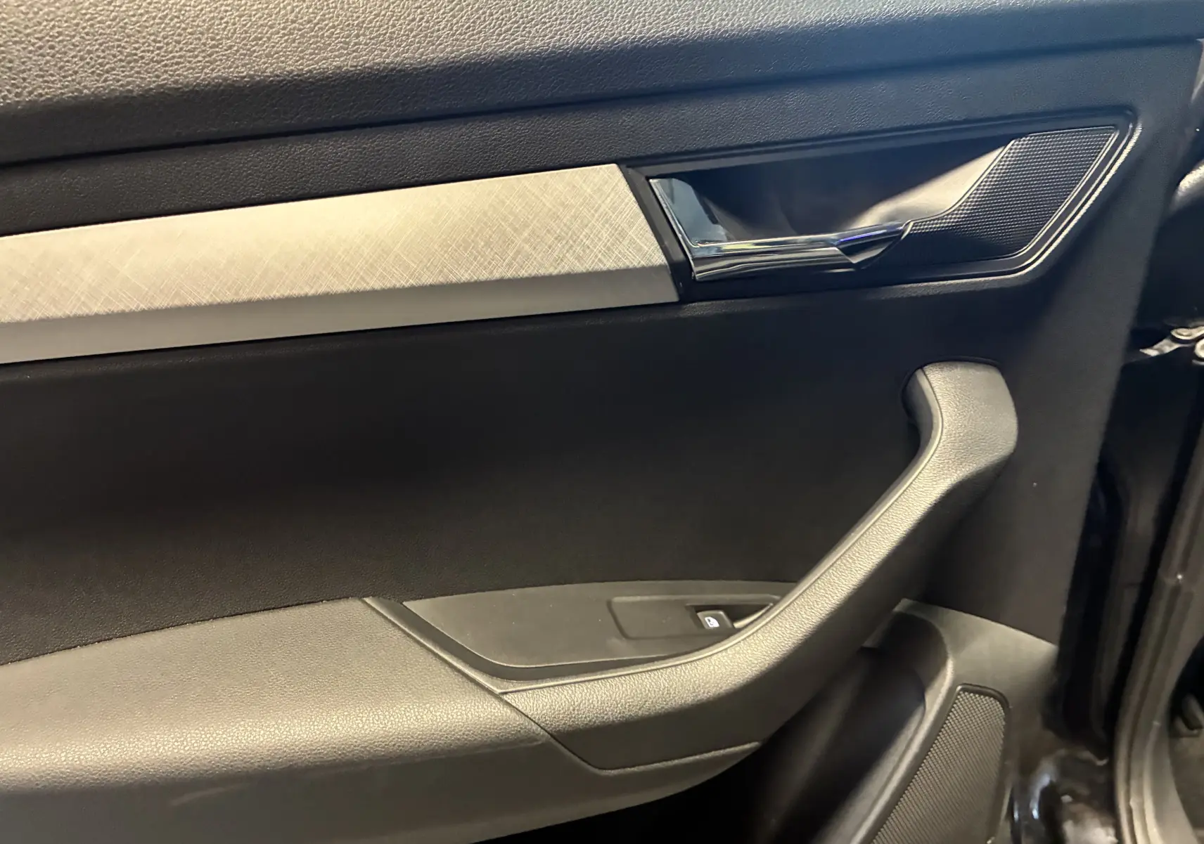 Détail de la porte intérieure droite noire du Skoda Karoq 2.0 TDI 116 DSG7 Business avec poignée chromée et insert décoratif argenté.