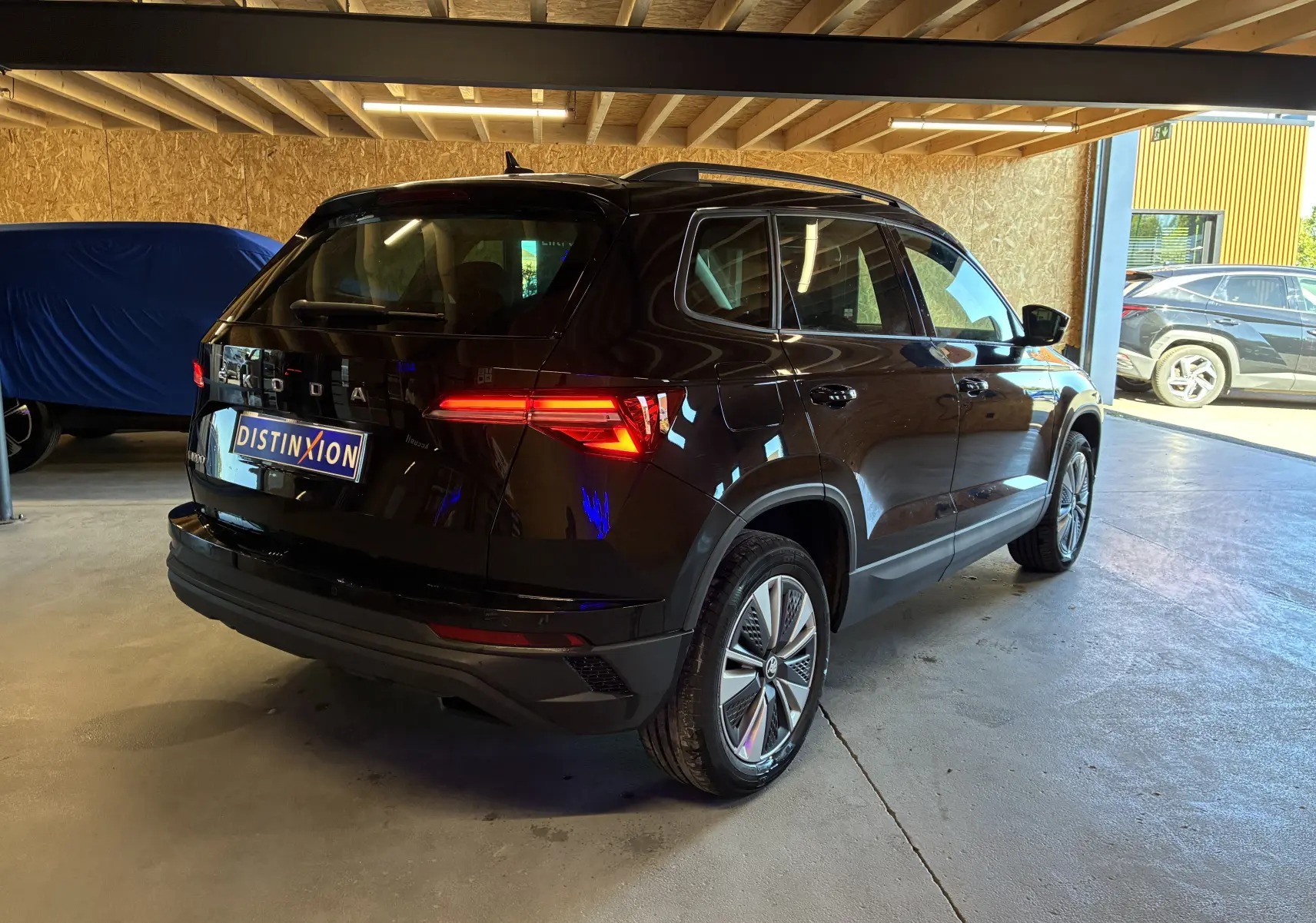 Vue 3/4 arrière droite d'un Skoda Karoq noir 2024 avec jantes alliage 17'' et feux arrière LED allumés.