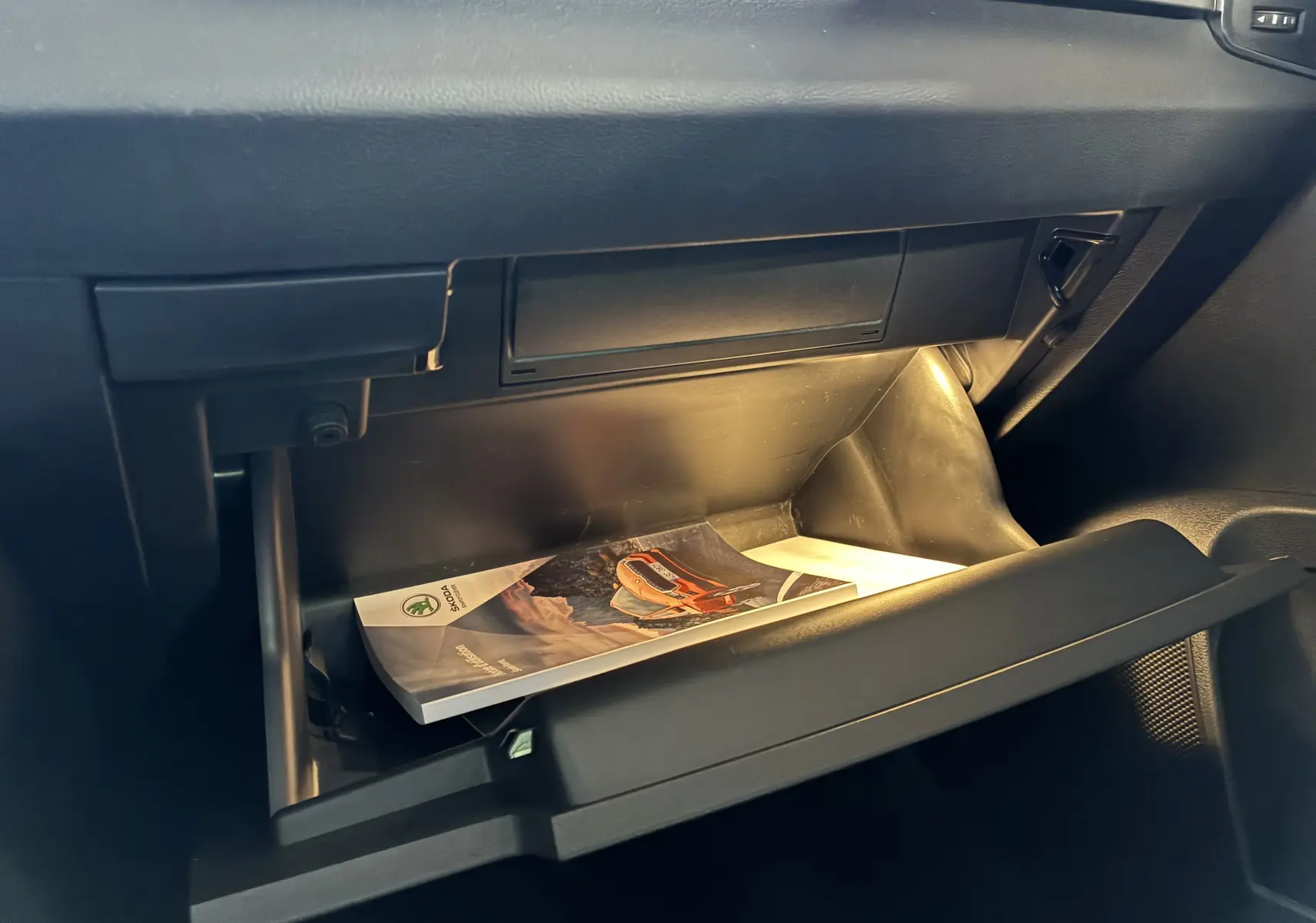 Gant de boîte à gants ouvert avec manuel Skoda KAROQ 2.0 TDI 116 DSG7 Business visible, intérieur noir.