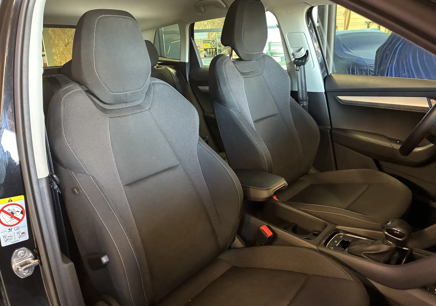 Vue intérieure côté conducteur de la Skoda Karoq noire 2024, sièges tissu noirs avec console centrale et boîte auto DSG7.