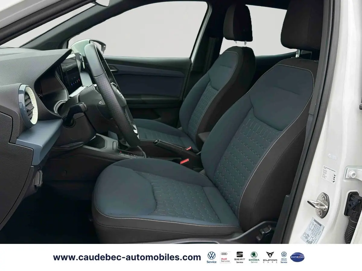 Vue intérieure côté conducteur du SEAT Arona blanc 2026, montrant les sièges avant en tissu gris et volant cuir multifonction.