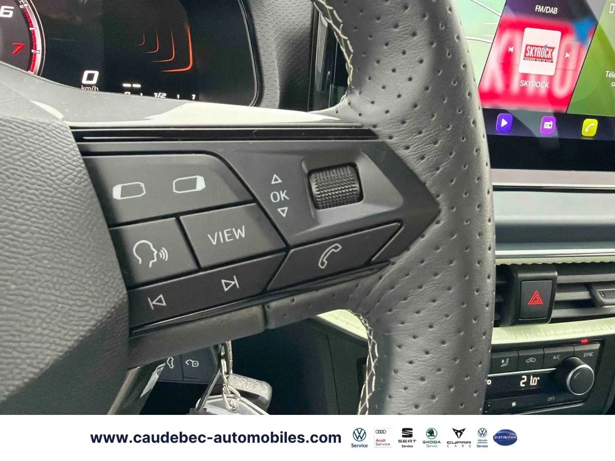 Gros plan sur le volant en cuir perforé de la SEAT Arona blanche, avec commandes multifonctions et écran tactile visible.