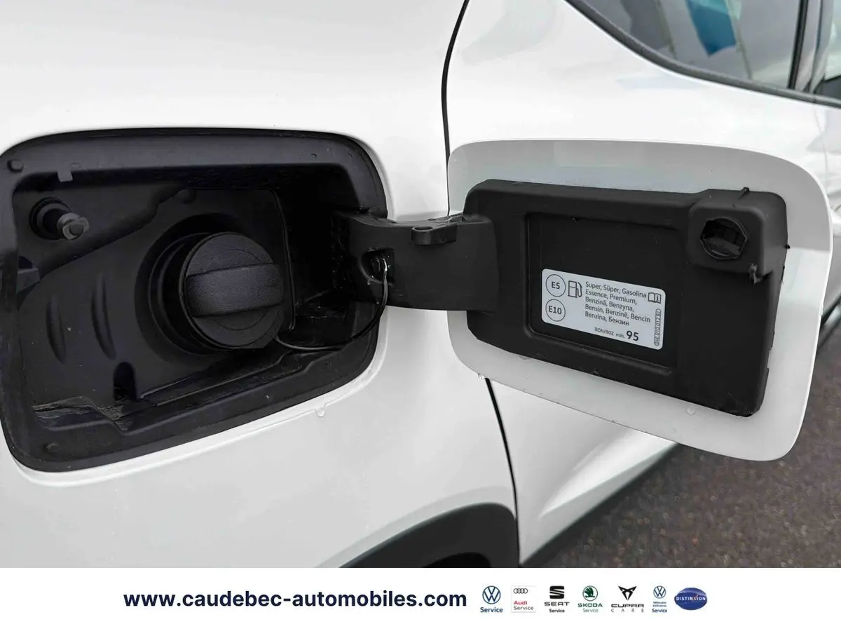 Vue rapprochée de la trappe à carburant ouverte côté gauche d’une SEAT Arona blanche, avec bouchon essence visible.