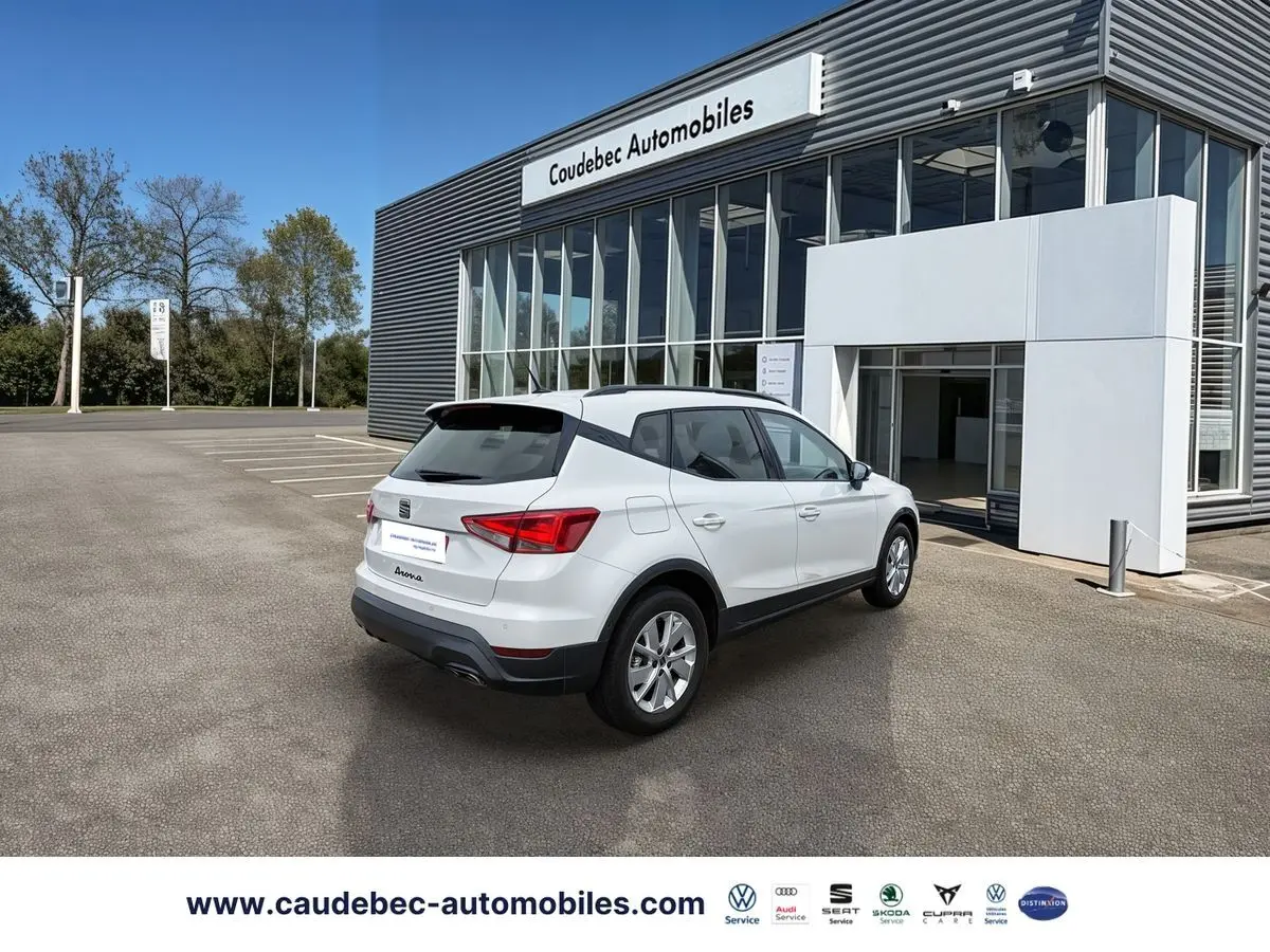 Vue 3/4 arrière droite d’un SEAT Arona blanc stationné devant un bâtiment moderne avec jantes alliage 16 pouces.