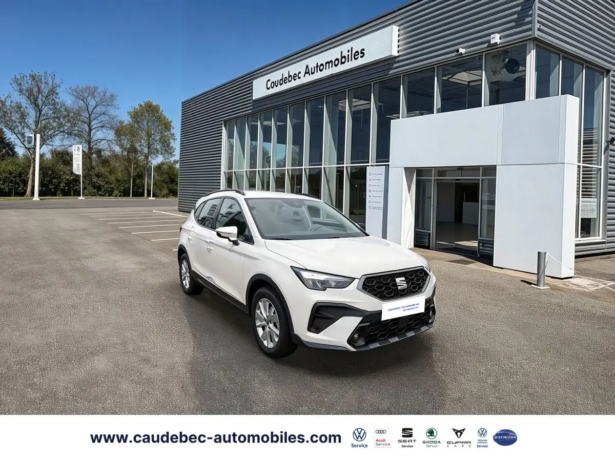 SEAT Arona blanc en 3/4 avant droit devant un bâtiment de concession avec jantes alliage 16 pouces design.