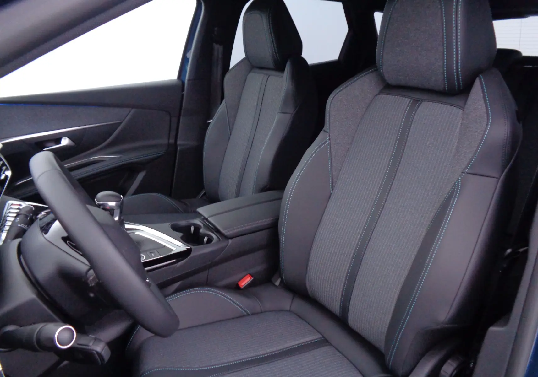 Vue intérieure côté conducteur du Peugeot 3008 2023, sièges en tissu gris et cuir noir avec surpiqûres bleues.