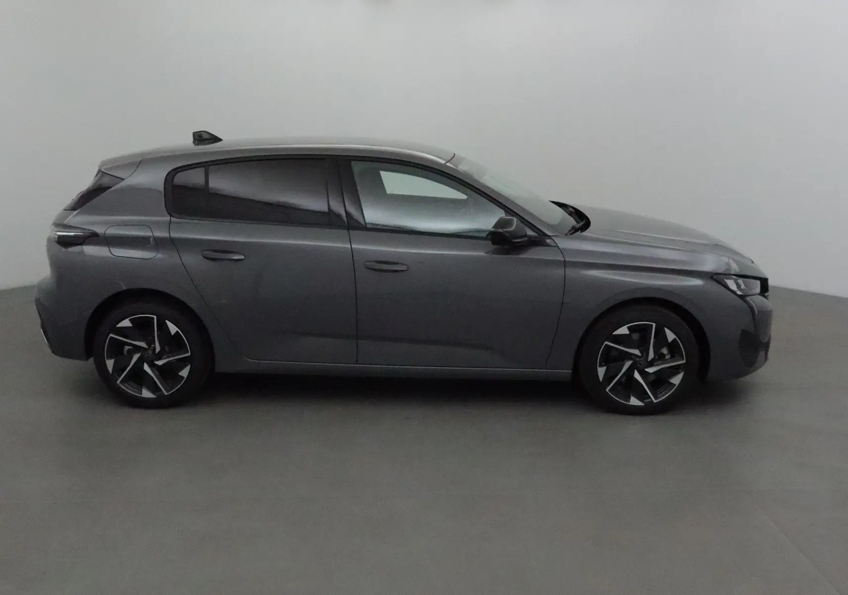 Profil côté gauche d'une Peugeot 308 gris selenium avec jantes alliage et vitres teintées dans un studio.