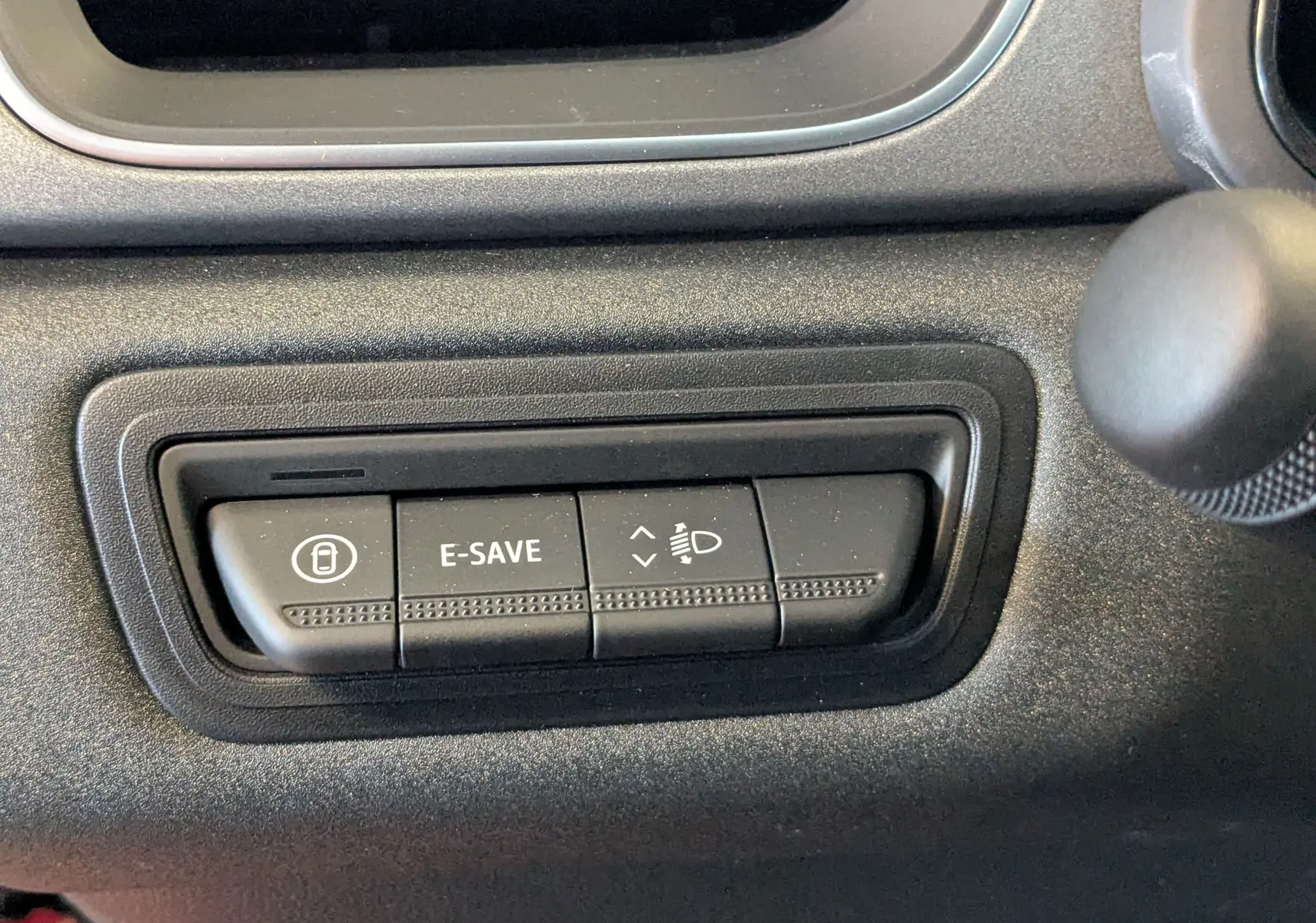 Gros plan sur les boutons de commande E-SAVE et réglage des phares du tableau de bord du Renault Captur hybride 2025.
