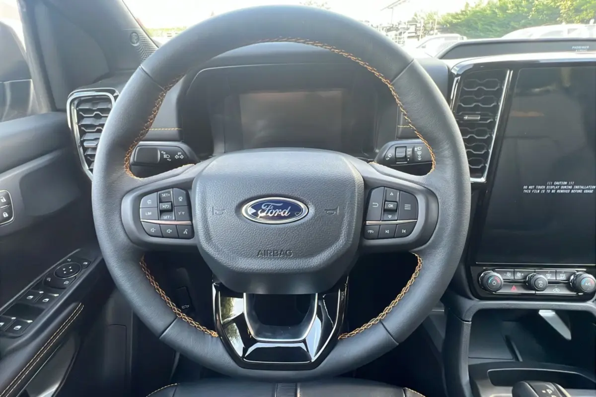Volant cuir noir avec surpiqûres marron et commandes multifonctions du Ford Ranger 2025, tableau de bord et écran tactile visibles.