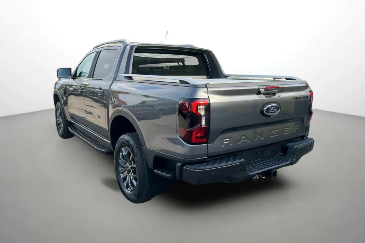 Ford Ranger 3.0 V6 Wildtrak Plus gris carbone vu 3/4 arrière droit avec benne et barres de toit visibles.