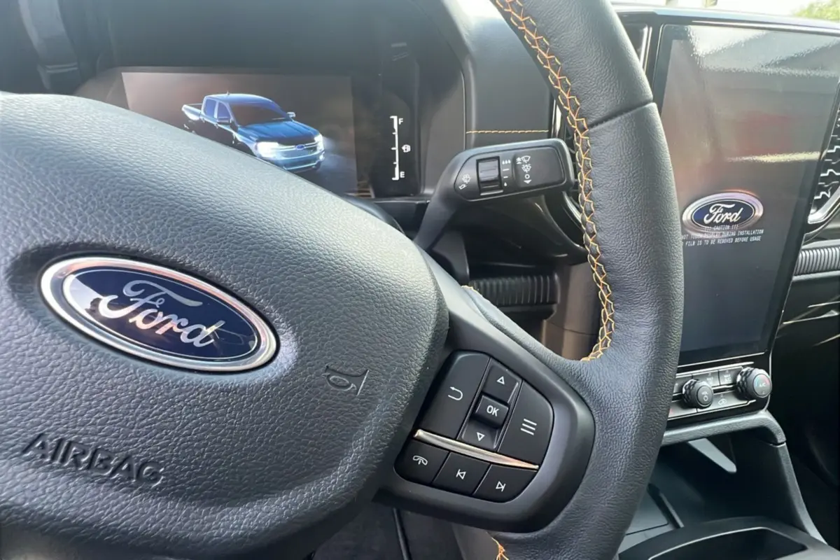 Gros plan sur le volant en cuir noir avec surpiqûres orange du Ford Ranger Wildtrak 2025 et écran central tactile.