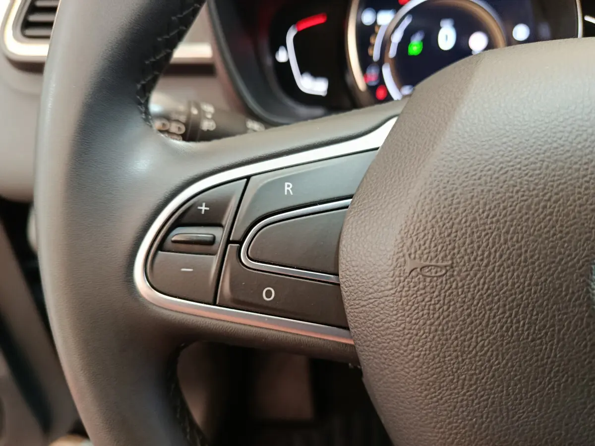 Gros plan sur les commandes du volant noir du Renault Kadjar Business gris foncé, avec tableau de bord lumineux en arrière-plan.