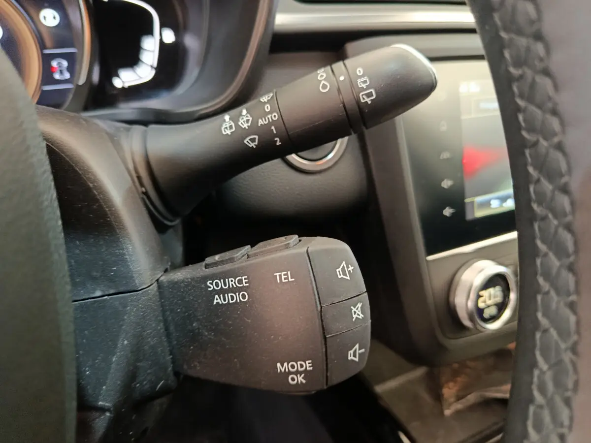 Gros plan sur la commande audio au volant d'un Renault Kadjar gris foncé, avec tableau de bord et écran tactile en arrière-plan.